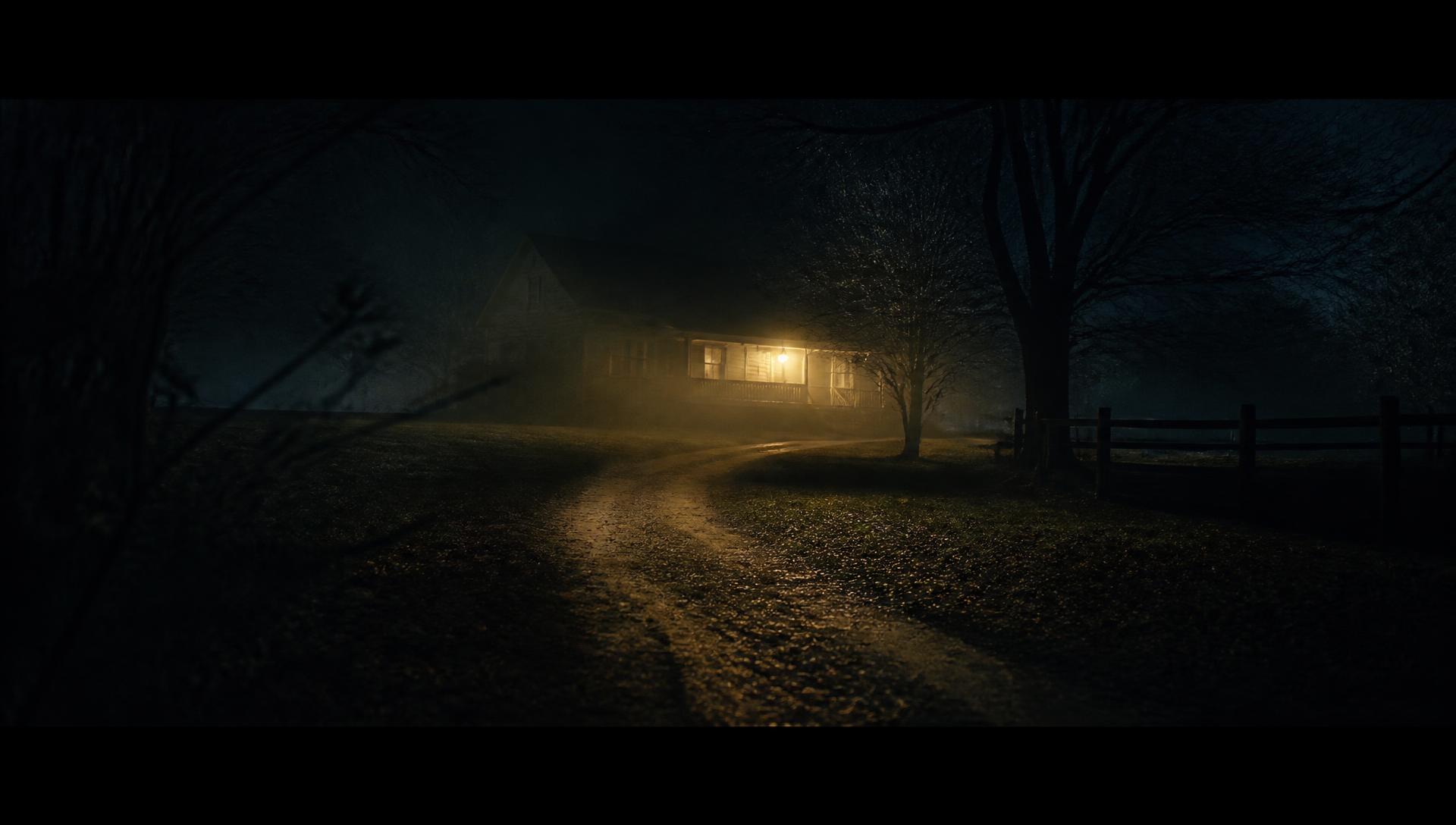 A fog-covered driveway at night leading to a house with a single porch light